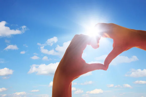 hands of a woman and a heart shape of a hand on a blue sky background