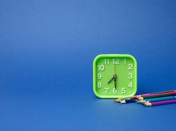 Reloj Verde Cuadrado Pila Lápices Madera Multicolores Sobre Fondo Azul — Foto de Stock