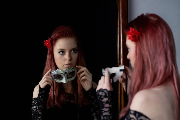魅力的な赤毛の若い女性は 鏡のカーニバルマスクを保持自分自身を見ている 水平方向 — ストック写真