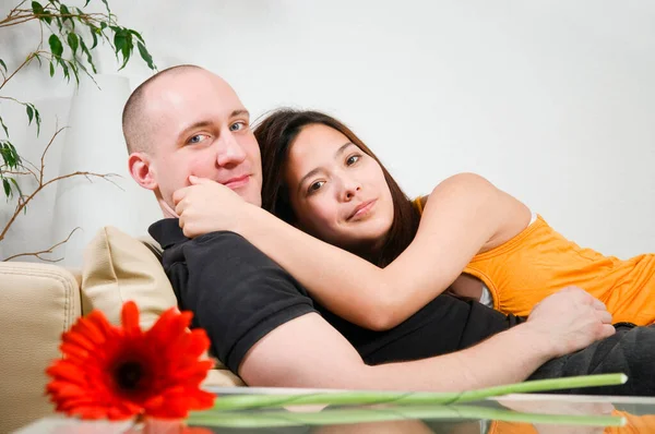 明るい壁の前に家でソファに抱きついている若い異性のカップルの二重の肖像画をリクライニングカメラを見て — ストック写真