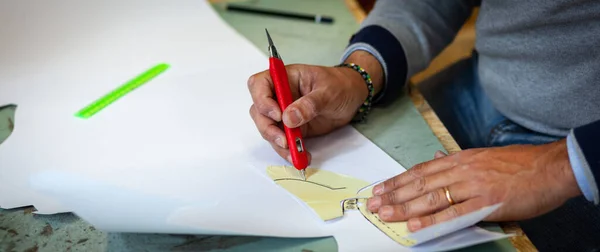 Shoemaker or shoe designer working with lwith paper models for leather cutting.