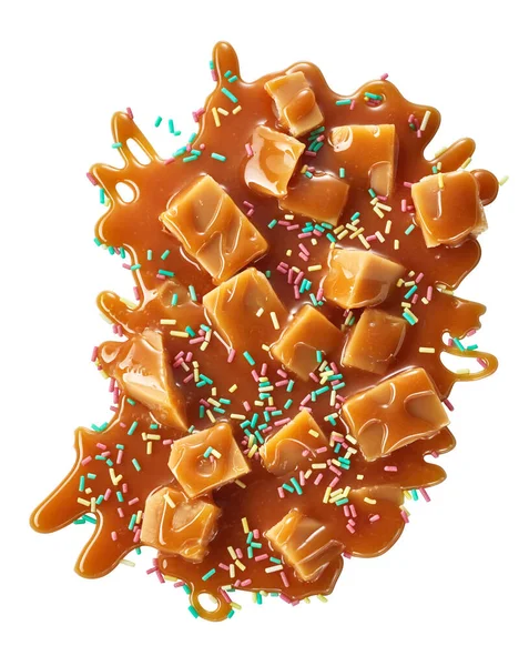 Splash of caramel sauce with fudge candies and sprinkles topping. Top view of sweet treat portion isolated on white background