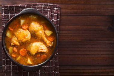 Fresh homemade chicken stew with potato, carrot and celery, seasoned with paprika in rustic bowl, photographed overhead with copy space on the side clipart