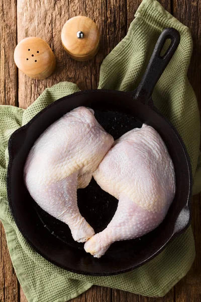 Fresh raw chicken thighs in cast-iron skillet, salt and pepper shakers on the side, photographed overhead (Selective Focus, Focus on the meat)