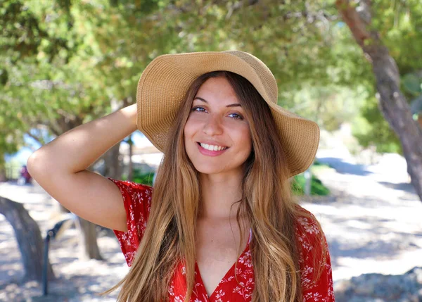 一个美丽的微笑的女孩穿着红色礼服和草帽看着相机的肖像 — 图库照片