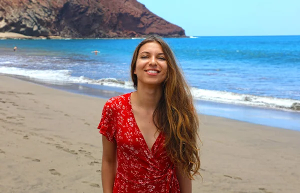 美丽的微笑的女人走在沙滩上 并摆出红色礼服 — 图库照片
