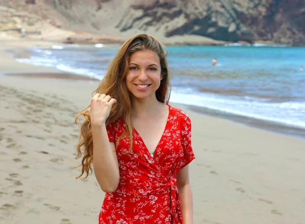 美丽的微笑的女人走在沙滩上 并摆出红色礼服 — 图库照片