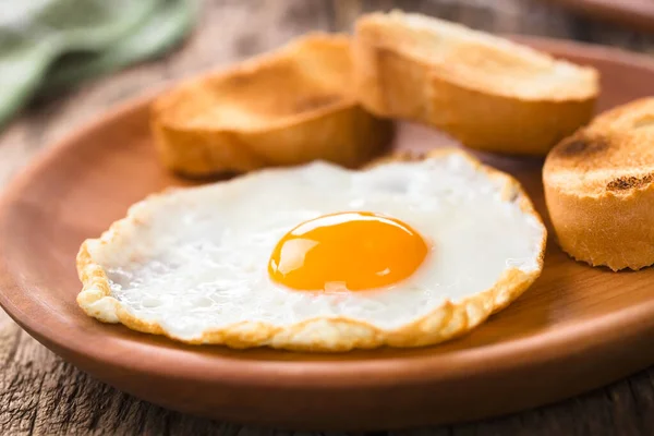 一个新鲜的煎蛋 一面阳光明媚 一面是烤面包片 一面是木制盘子 选择性聚焦 集中在蛋黄的正面 — 图库照片