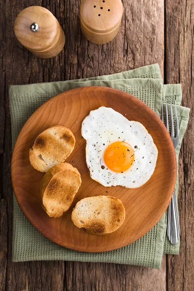 一个新鲜的煎蛋 阳光明媚的一面 烤面包片放在旁边 放在木制盘子上 头顶上拍照 选择性聚焦 专注于鸡蛋 — 图库照片