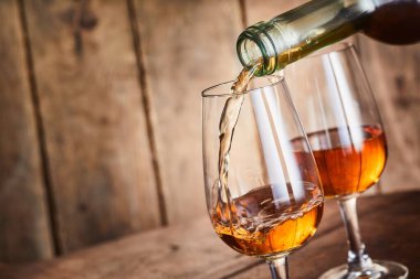 Aged golden fortified Spanish sherry being poured into stylish glasses in a close up on the neck of the bottle over wood with copy space at a tilted angle clipart