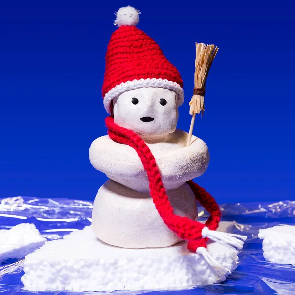 A snowman with a red scarf and red bobble hat on a small ice floe in the sea.