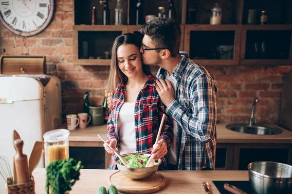 年轻的丈夫在厨房亲吻他的妻子 而她做饭早餐 男人和女人一起准备蔬菜沙拉 快乐的家庭在一起 — 图库照片