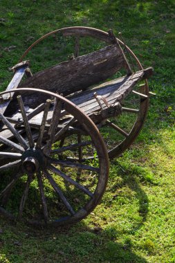 Güneşin aydınlattığı yeşil çimlerin üzerinde terk edilmiş eski ahşap bir araba.