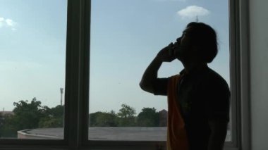 Pencere arkasında telefonla konuşan bir adamın silueti 