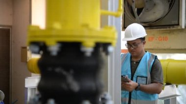 Kazan dairesinde çalışan Asyalı mühendis, ısıtma sistemi ekipmanlarının teknik verilerini kontrol ediyor.