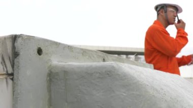 Fabrikanın çatısında pano kontrol ekipmanlarıyla erkek mühendis müfettişi radyo setinde konuşuyor.