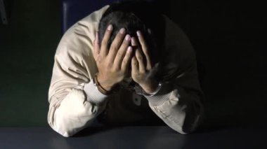 Erkek mahkum karakolda sorgu odasında oturuyor.