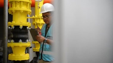 Kazan dairesinde çalışan Asyalı mühendis, ısıtma sistemi ekipmanlarının teknik verilerini kontrol ediyor.