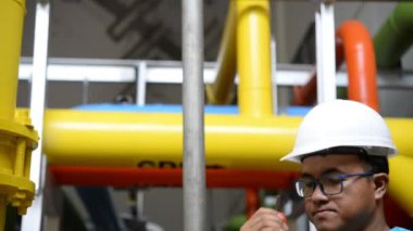 Kazan dairesinde çalışan Asyalı mühendis, ısıtma sistemi ekipmanlarının teknik verilerini kontrol ediyor.