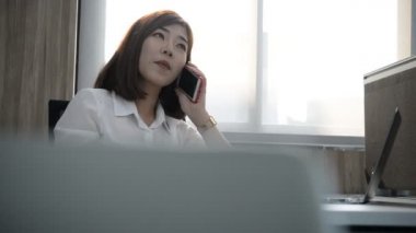 Ofiste çalışırken akıllı telefondan konuşan Asyalı iş kadını.