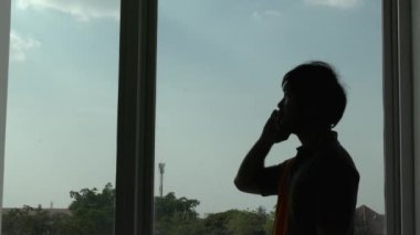 Pencere arkasında telefonla konuşan bir adamın silueti 
