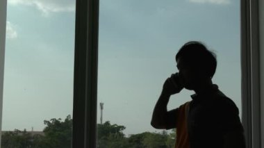 Pencere arkasında telefonla konuşan bir adamın silueti 