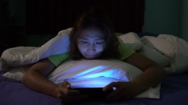 Asyalı kadın gece yatakta akıllı telefonla oyun oynuyor.