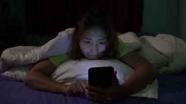 Asyalı kadın gece yatakta akıllı telefonla oyun oynuyor.