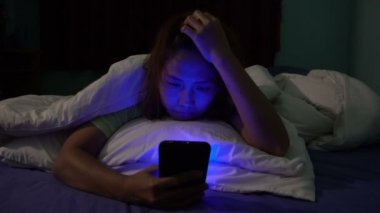 Asyalı kadın gece yatakta akıllı telefonla oyun oynuyor.