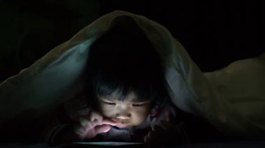 Küçük tatlı Asyalı kız yatakta yatarken akıllı telefonuyla oynuyor. 