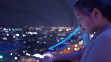 Gece gözetleme kulesinde dikilirken akıllı telefon kullanan Asyalı kadın. 