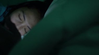 Asyalı kadın gece yatakta akıllı telefonla oyun oynuyor.