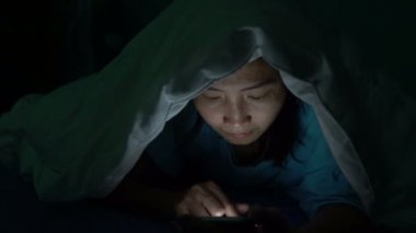 Asyalı kadın gece yatakta akıllı telefonla oyun oynuyor.