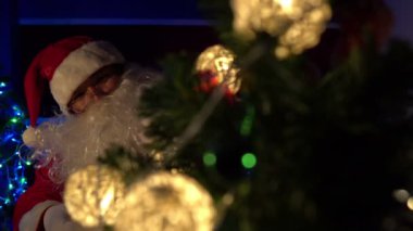 Noel Baba 'nın Noel ağacını çelenkle süslemesi, mutlu bayramlar.