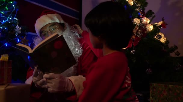 Santa Läsa Bok Med Liten Pojke Nära Julgran Med Girland — Stockvideo