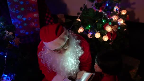 Livre de lecture du Père Noël avec petit garçon près de l'arbre de Noël avec guirlande, concept de vacances heureuses 