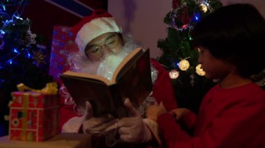 Noel Baba, Noel ağacının yanında çelenk taşıyan küçük bir çocukla kitap okuyor. Mutlu Noeller konsepti.