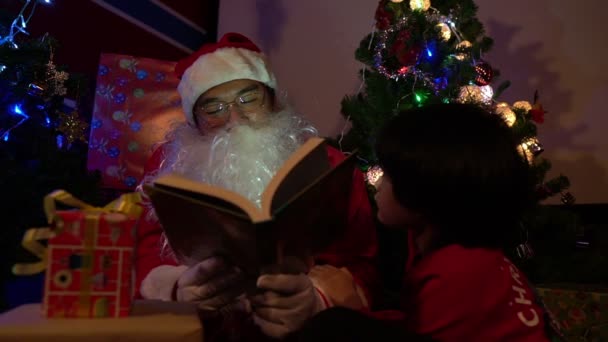 Книга Санта Клауса Маленьким Мальчиком Возле Елки Гирляндой Концепция Счастливого — стоковое видео