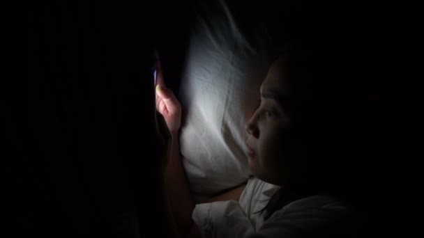アジアの女性は夜にベッドでスマートフォンを再生します タイの人々 — ストック動画