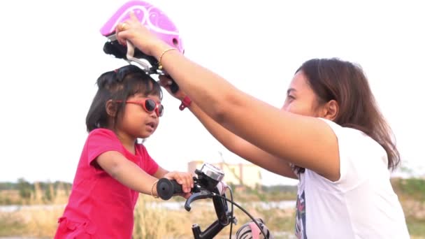 幼い娘の頭にヘルメットをかぶるお母さん屋外で自転車に乗っている女の子 — ストック動画