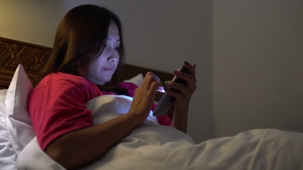 アジアの女性は夜にベッドでスマートフォンを再生します — ストック動画