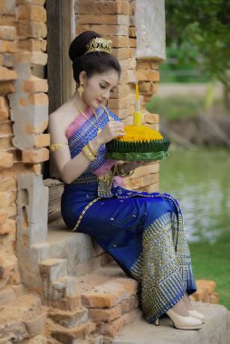 Tayland elbisesi giymiş güzel Asyalı bir kadının portresi geleneksel dua Kratong 'u loy kratong festivaline katılması için tutuyor.