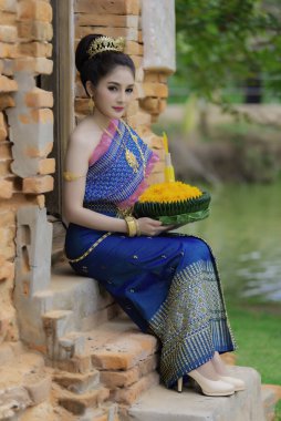 Tayland elbisesi giymiş güzel Asyalı bir kadının portresi geleneksel dua Kratong 'u loy kratong festivaline katılması için tutuyor.