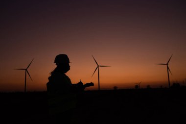 Kadın mühendisin silueti rüzgar türbini çiftliği elektrik jeneratörü istasyonunda çalışıyor ve raporu tutuyor.