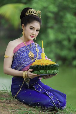 Tayland elbisesi giymiş güzel Asyalı bir kadının portresi geleneksel dua Kratong 'u loy kratong festivaline katılması için tutuyor.