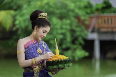 Tayland elbisesi giymiş güzel Asyalı bir kadının portresi geleneksel dua Kratong 'u loy kratong festivaline katılması için tutuyor.