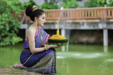 Tayland elbisesi giymiş güzel Asyalı bir kadının portresi geleneksel dua Kratong 'u loy kratong festivaline katılması için tutuyor.