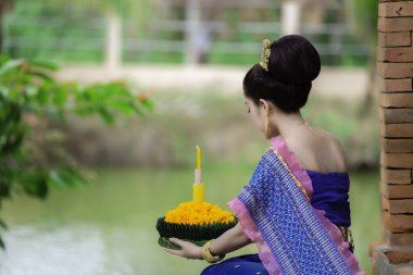 Tayland elbisesi giymiş güzel Asyalı bir kadının portresi geleneksel dua Kratong 'u loy kratong festivaline katılması için tutuyor.