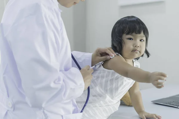 亚洲医生用听诊器检查一个可爱女孩的呼吸和心脏 — 图库照片