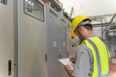 Kazan dairesinde çalışan gözlüklü Asyalı mühendis ısıtma sistemi ekipmanlarının teknik verilerini kontrol ediyor.